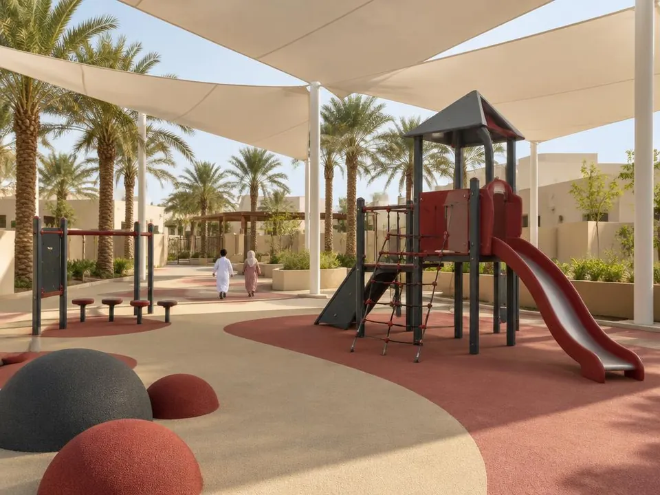 Shaded outdoor playground with a slide, climbing frame and palm trees